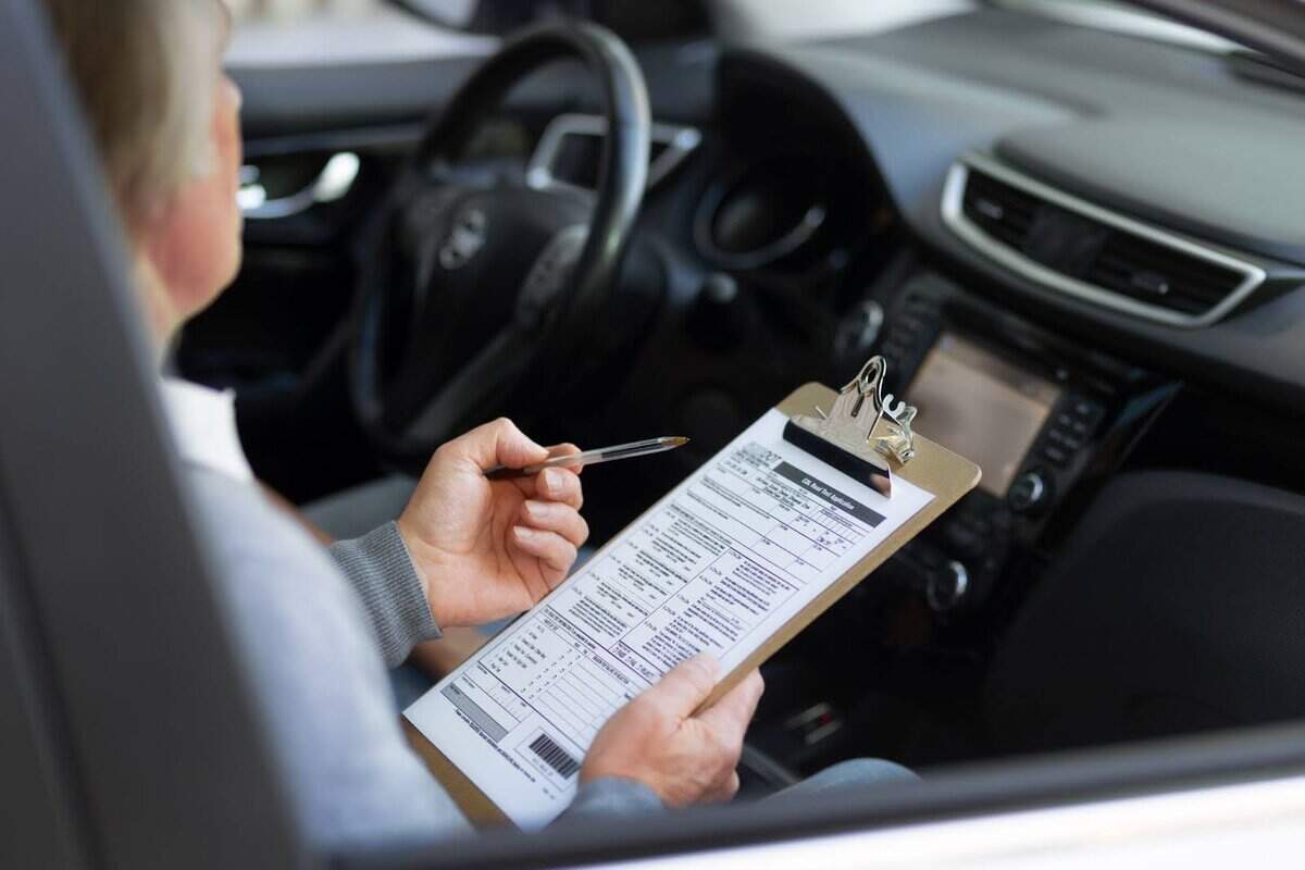 Femme assis dans une voiture, tenant un stylo dans sa main gauche et de sa main droite une feuille montrant les papiers (historique) d’une voiture